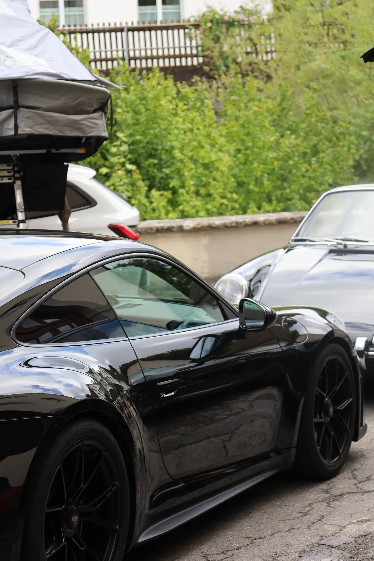 Schwarzer Porsche in Seitenansicht, dahinter ein Klassiker